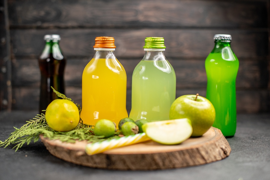 front-view-fruit-juice-in-bottles-apple-lemon-feijoas-pipettes-on-wood-board-lemonades-on-dark-surface